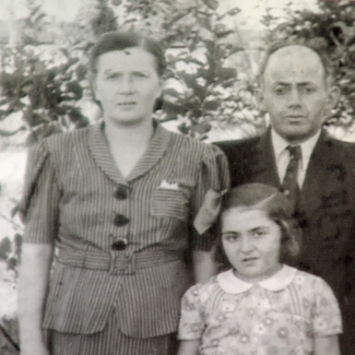 Photo en nir et blanc d'un homme et d'une femme avec leur jeune fille se tenant à l'extérieur où il y a des arbres en arrière-plan. L'homme porte un complet et la femme ainsi que la femme portent des blouses.