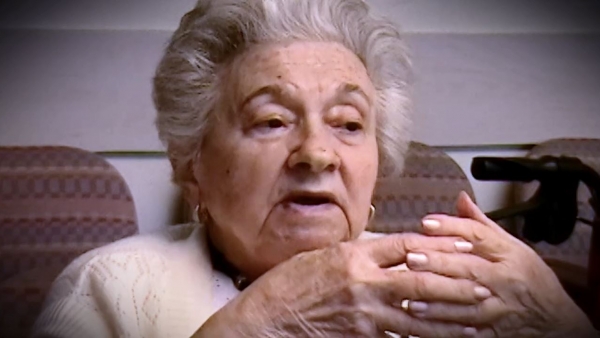 Capture d'écran du témoignage vidéo de la survivante de l’Holocauste Mania Kay, assise et regardant à la droite de la caméra. Son visage et ses épaules sont visibles à la caméra.